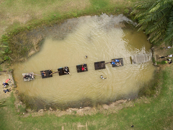 An aerial picture of a group of people helping each other to cross a bridge over a water surface.