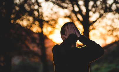 A man covering his face with his hands with trees in the background.