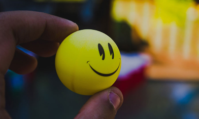 A person’s hand holding a small yellow ball with smiley face.