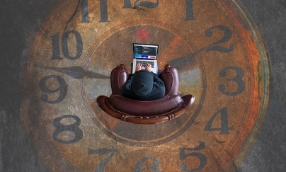 An aerial picture of a person sitting down on a leather chair, working on their laptop on their lap, with a clock artwork on the floor.