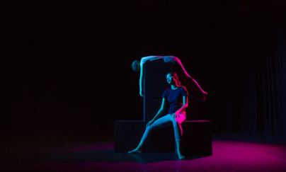 Two students performing a theatre performance where one student is sitting on a black cubicle and the other student is laying on another cubicle on top of the black cubicle at the Yale-NUS Black Box Theatre. 
