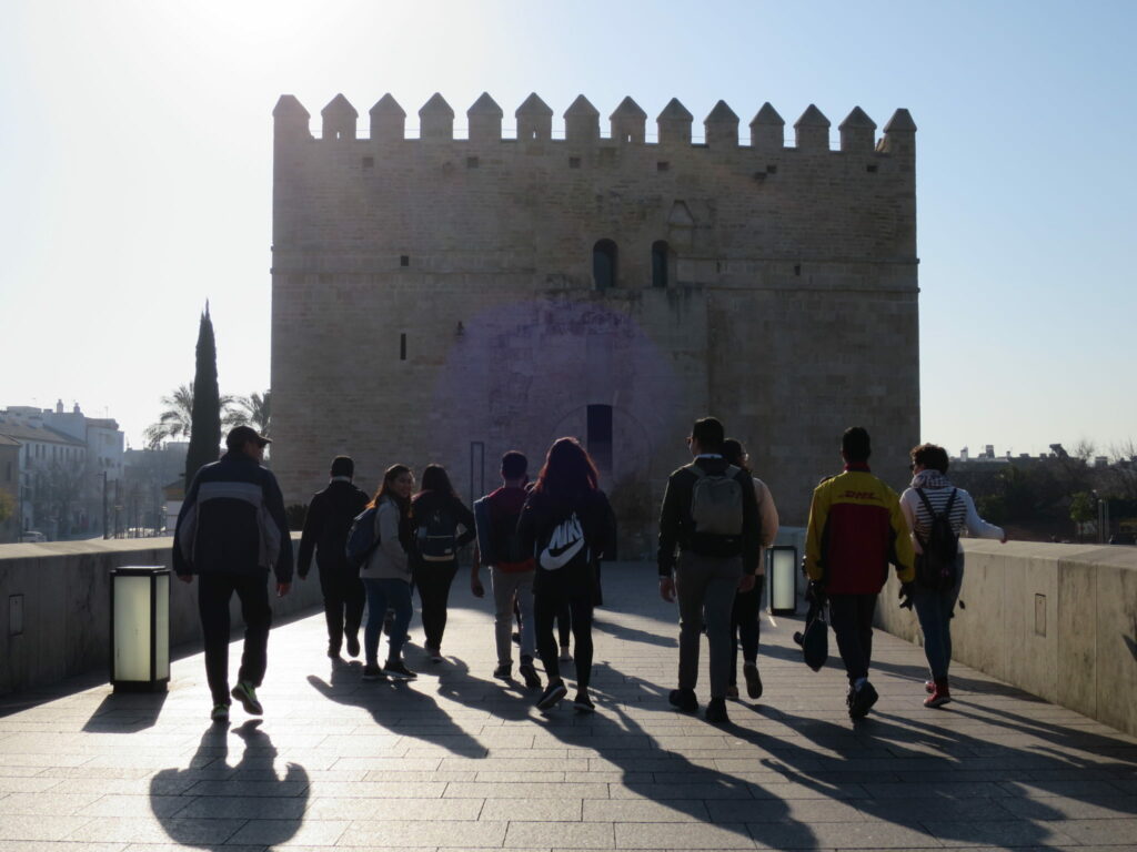 A back shot of a group of students walking on a bridge towards a castle.