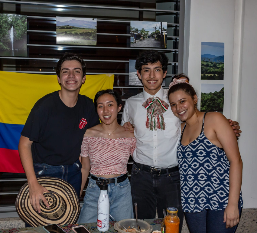 Four students embracing each other, posing for a photo with Columbia flag and scenery pictures in the background.