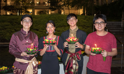 Four people posing in front of the Saga College Pond in the evening, each person holding a Krathong, celebrating the Loy Krathong festival at Yale-NUS. 