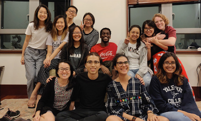 A group of students looking comfortable and some hugging each other, posing for a picture at a Rector’s Commons in the evening.