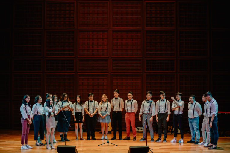 The Barbershop Choir performing on stage wearing the white t-shirt with black suspenders at the Yale-NUS Performance Hall.
