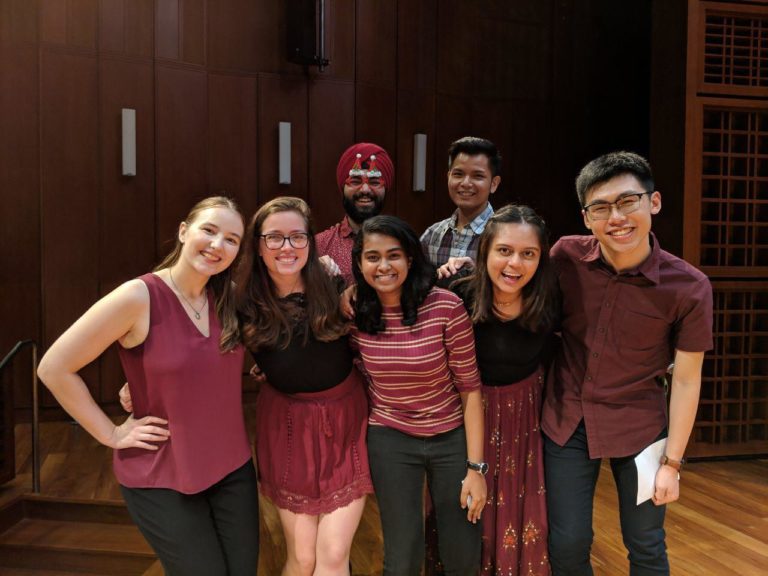 A group of seven students who is a part of the “Patchwork” acapella group, wearing a red-themed outfit posing for a picture at the Yale-NUS Performance Hall.