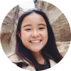 A self-portrait (or selfie) of smiling Betina Choa who has long black hair past her shoulders with rocks in the background.