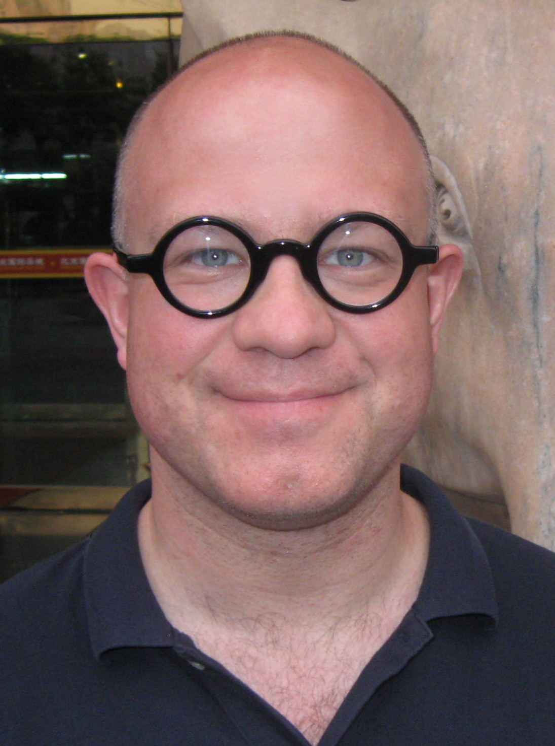 A headshot of smiling Matthew D Walker who is wearing round shaped glasses with a black frame and a dark blue polo shirt.