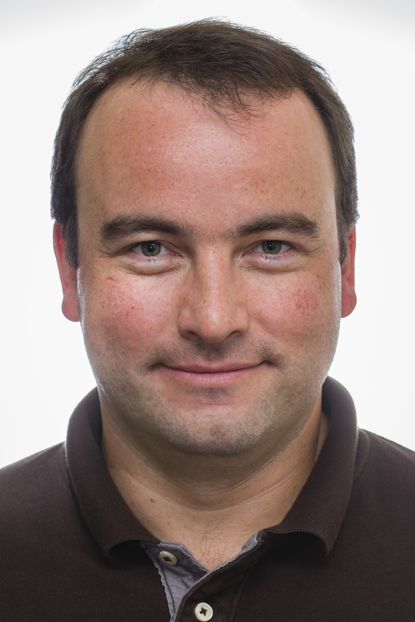 A headshot of smiling Nicholas Tolwinski who has short brown hair. He is wearing a brown polo shirt.