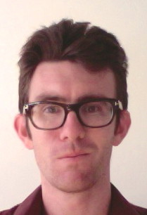 A headshot of smiling Steven Matthew Oliver who has short brown hair, wearing glasses with black frame and a maroon collared shirt.