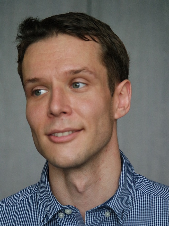 A headshot of smiling Andreas Heinecke who has short brown hair, wearing a checkered blue shirt.