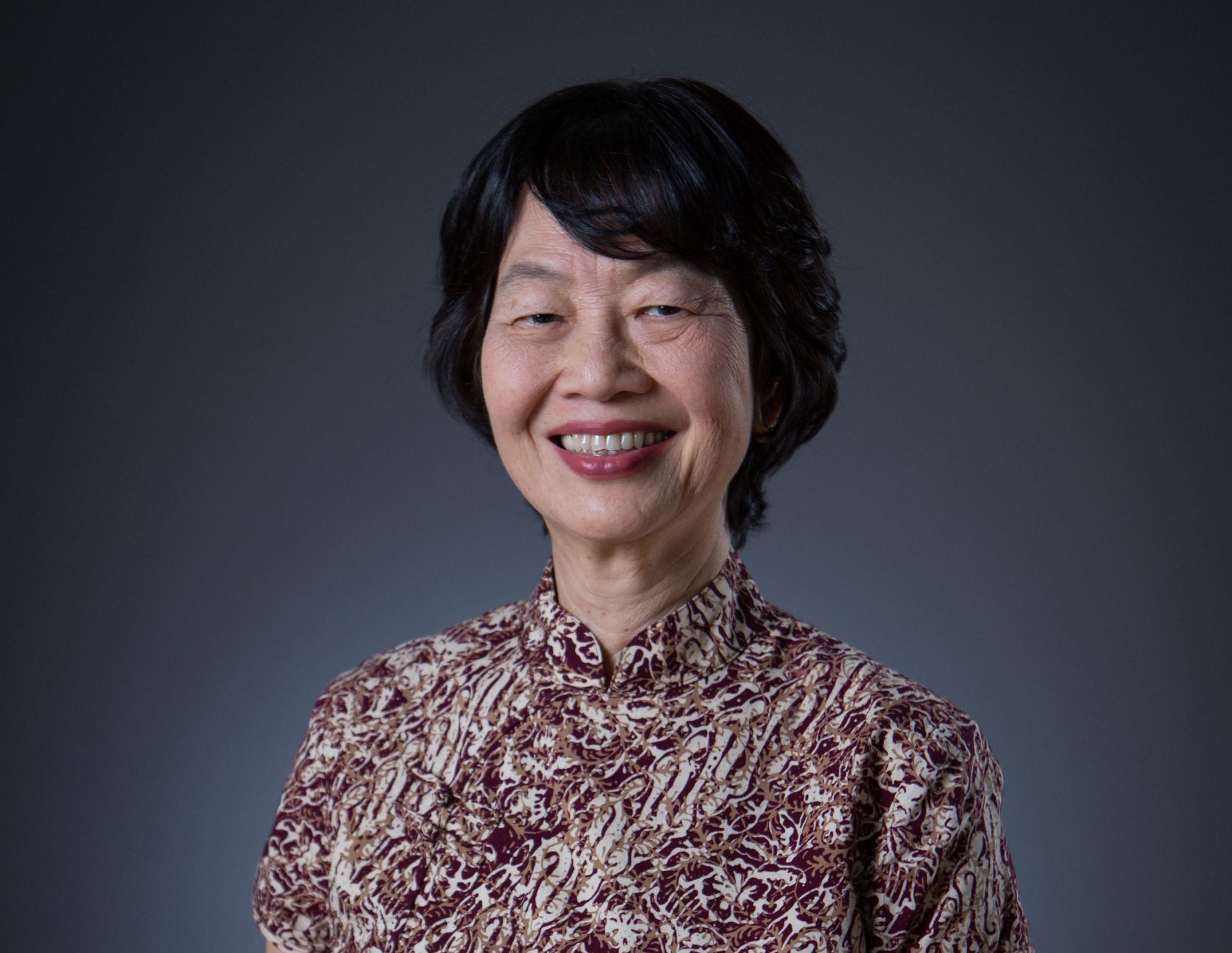 A headshot of smiling Hoon Eng Khoo who has short black hair and is wearing a red batik-patterned top.