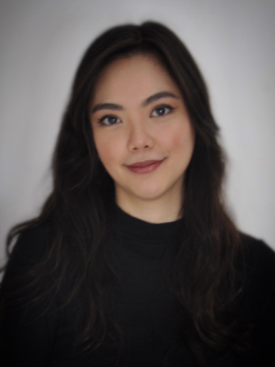 A headshot of smiling Christine Abigail Lee Tan who has wavy, long black hair, and is wearing a black turtleneck shirt.