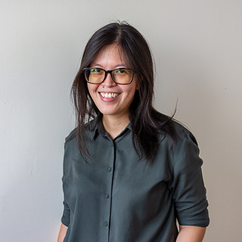 A headshot of smiling Tsin Yen Koh who has long black hair past her shoulders and is wearing glasses with a black frame and a black long sleeve collared shirt.